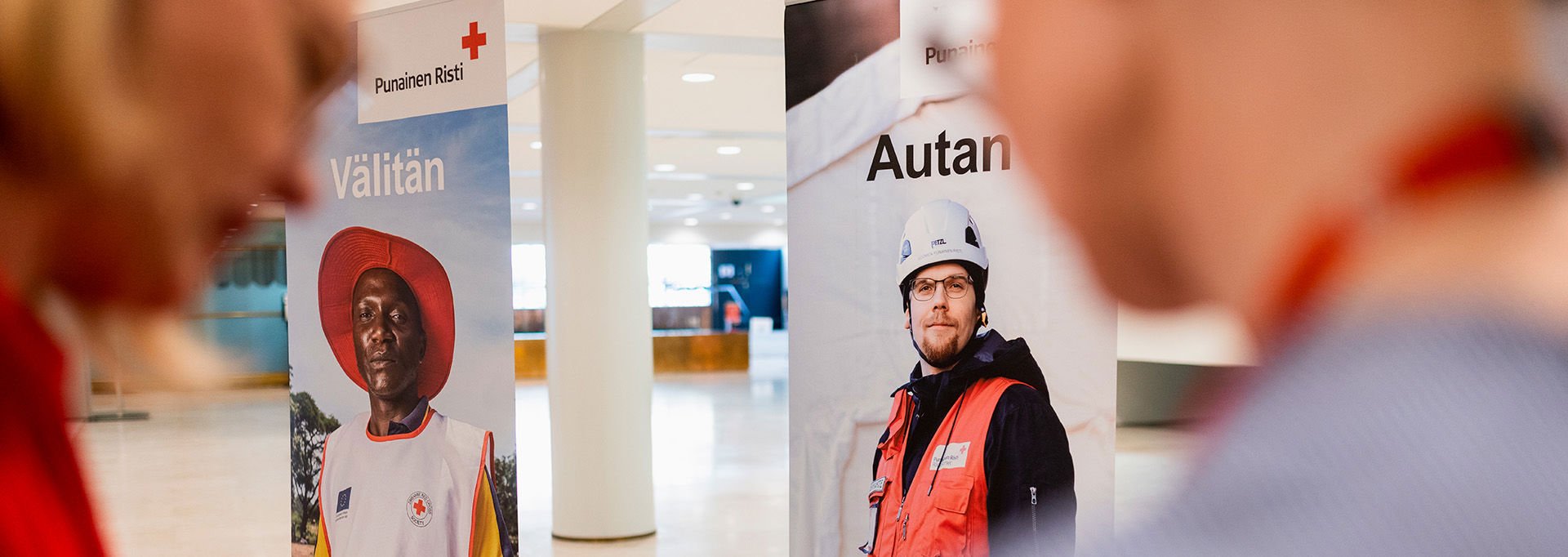 Två personer pratar. I bakgrunden finns två roll-ups med Röda Korsets volontärer.