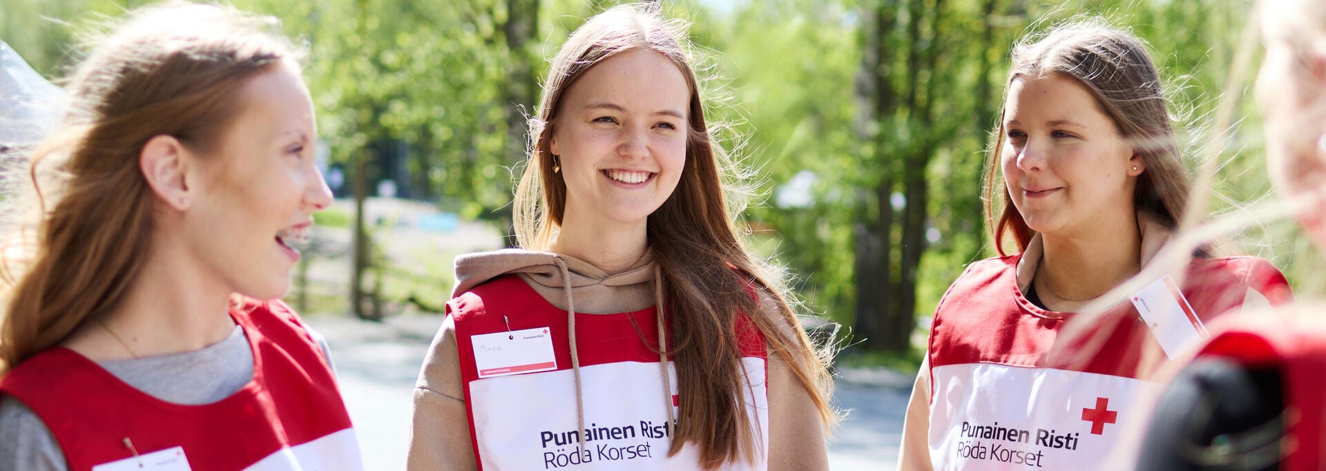 Röda Korsets frivilliga bössinsamlande volontärer ler utomhus i soligt väder.