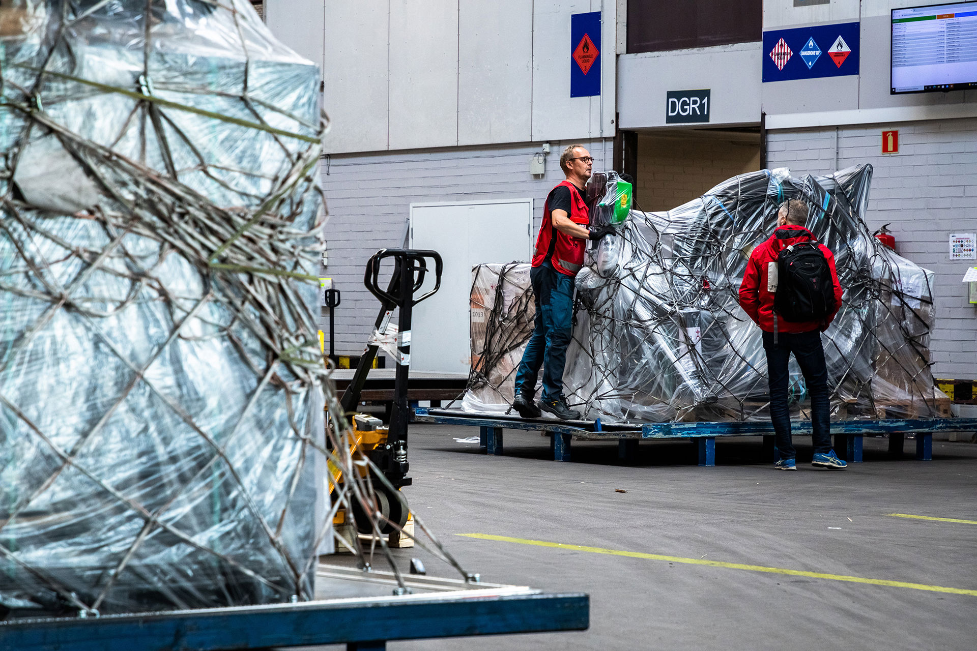 Två personer i Röda Korsets kläder packar stora lastpallar med gods på flygplatsen.