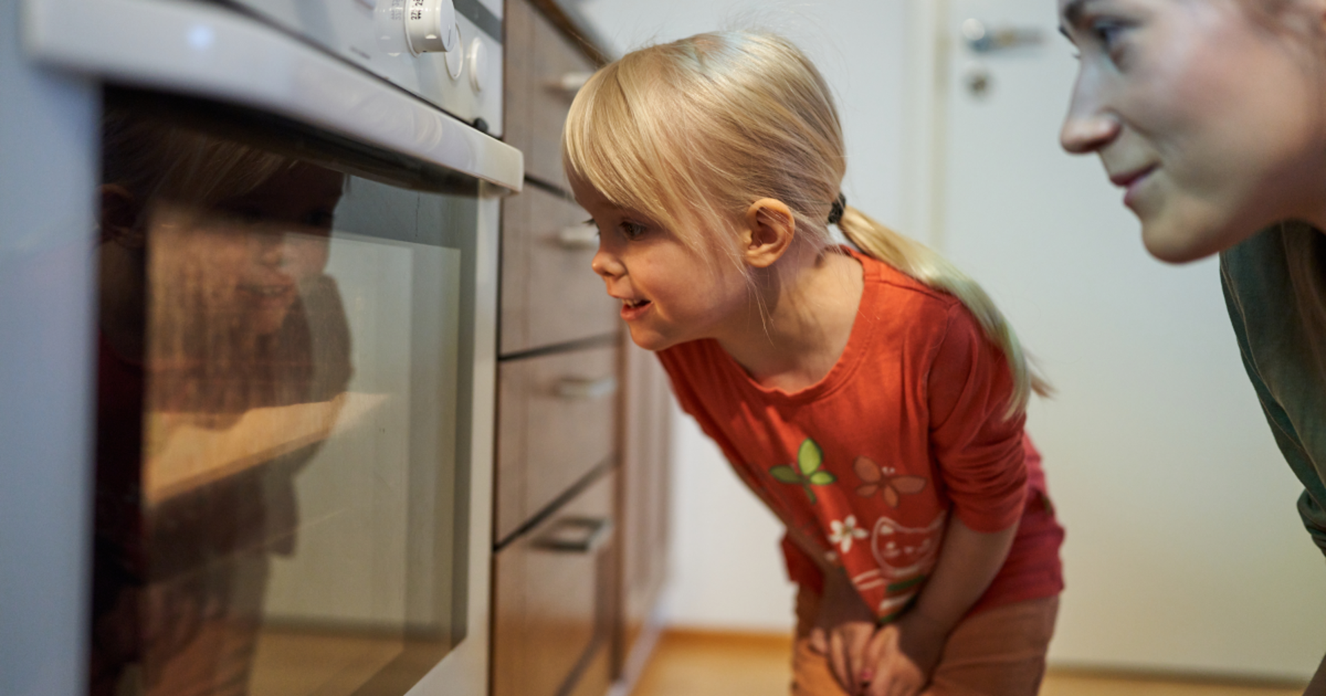 En mamma och sin dotter tittar  i ugnen om pepparkakor är färdiga.