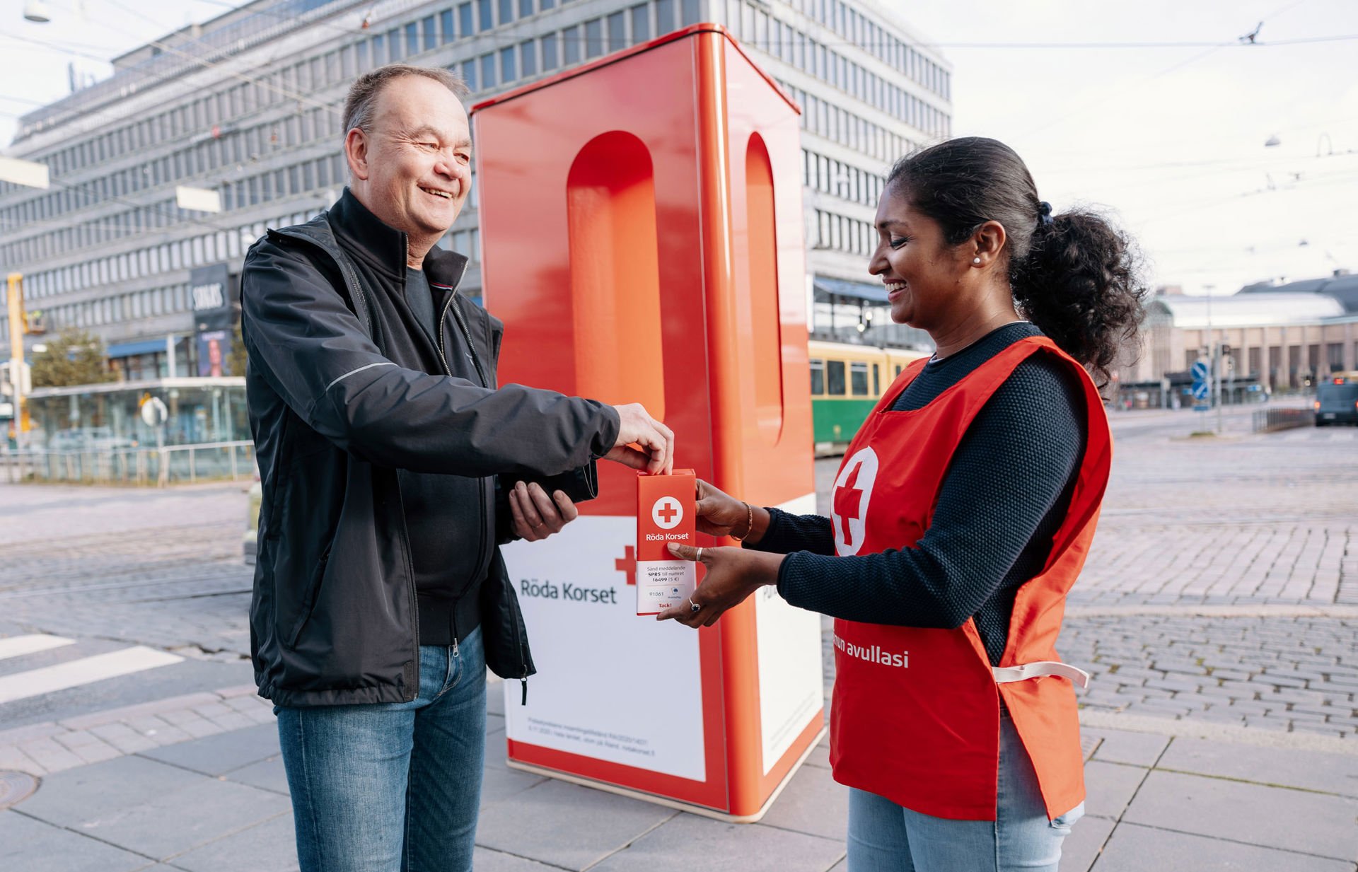 Leende bössinsamlare på hungerdagen räcker bössan till en leende givare.