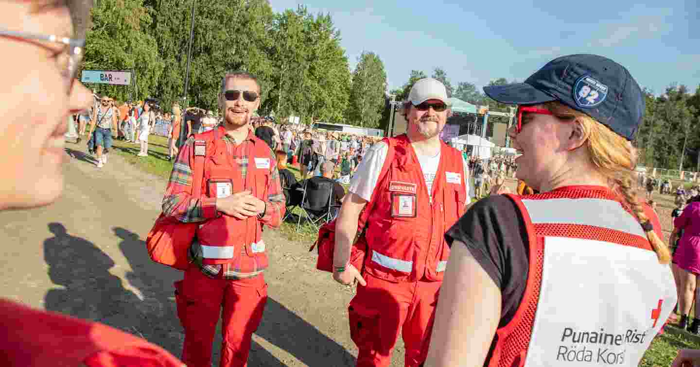 Fyra leende frivilliga från Röda Korset har jour i ett soligt festivalområde.