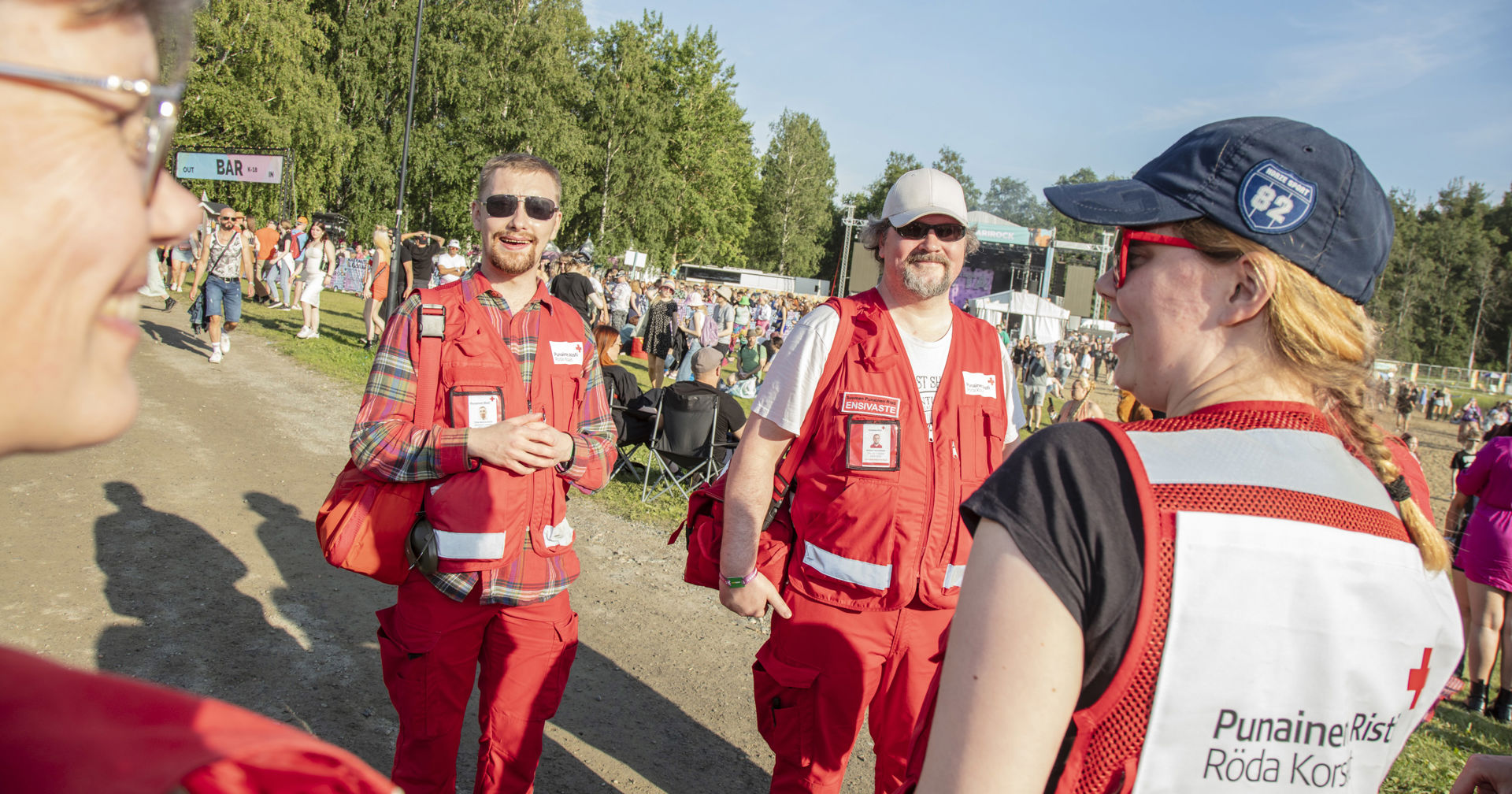 Fyra leende frivilliga från Röda Korset har jour i ett soligt festivalområde.