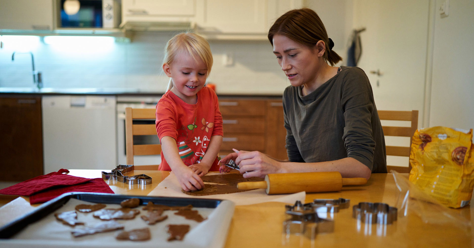 En mor och ett barn bakar pepparkakor i köket i sitt hem.