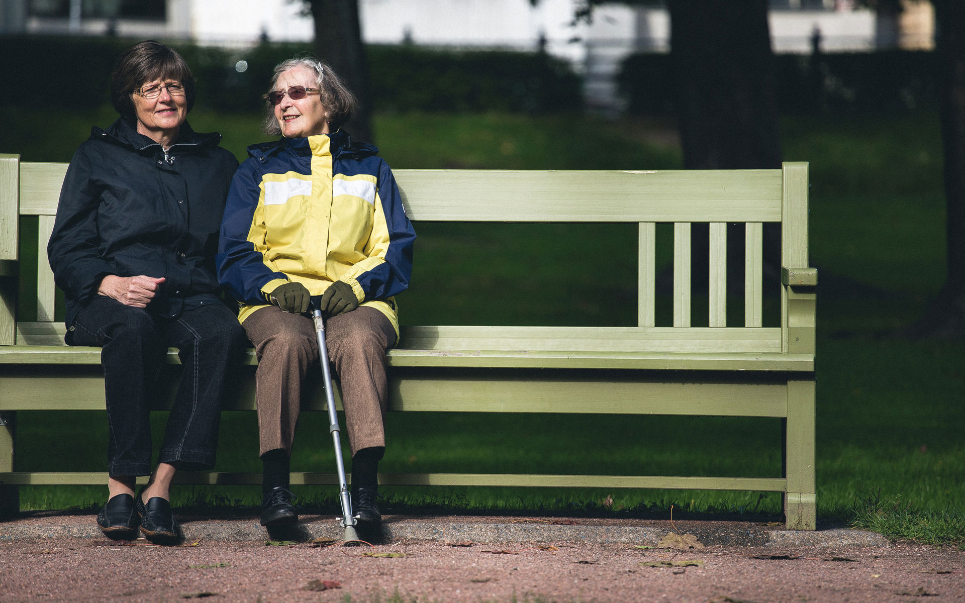 Två äldre kvinnor sitter bredvid varandra på en parkbänk.