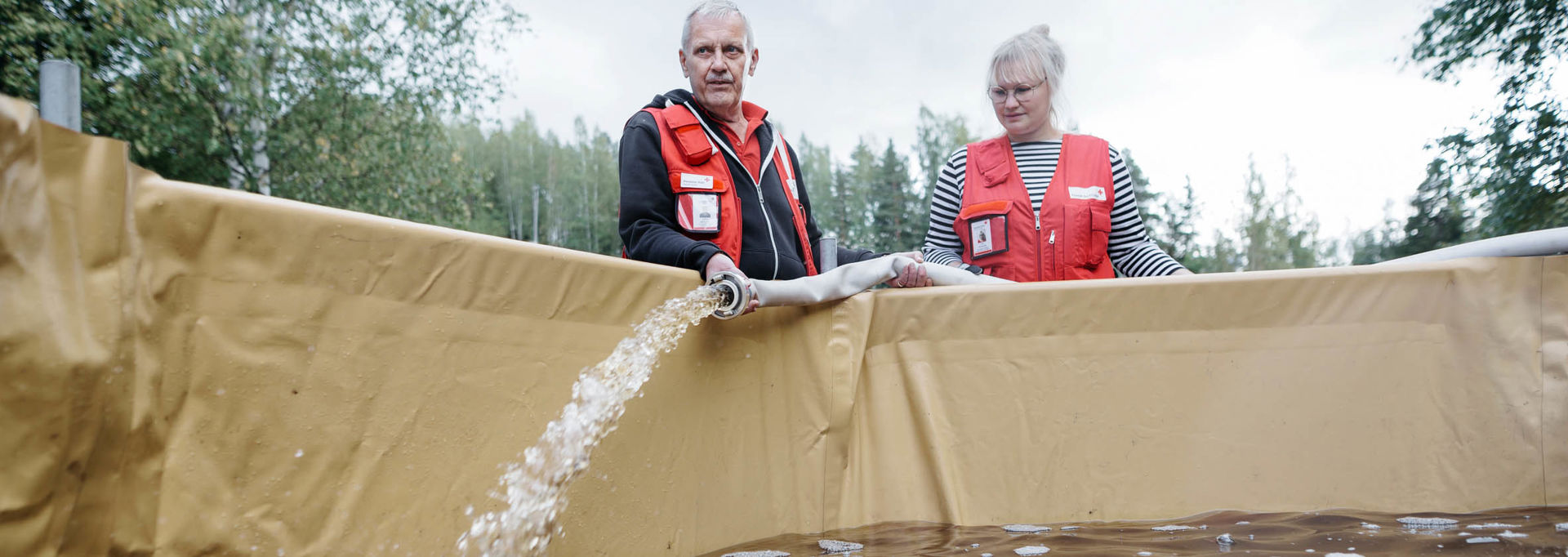 Nainen ja mies Punaisen Ristin varusteissa täyttävät vesiallasta puhtaalla vedellä.