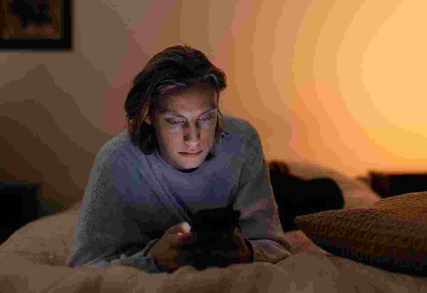 En person använder mobilen i sin säng i dunkel belysning.